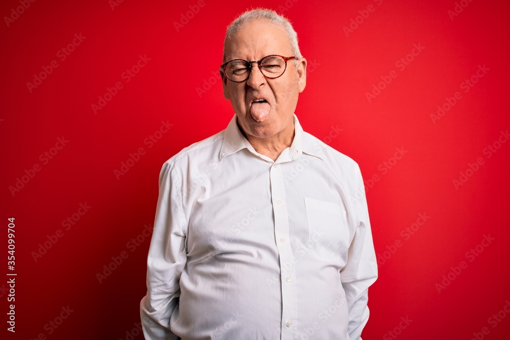 Middle age handsome hoary man wearing casual shirt and glasses over red background sticking tongue out happy with funny expression. Emotion concept.