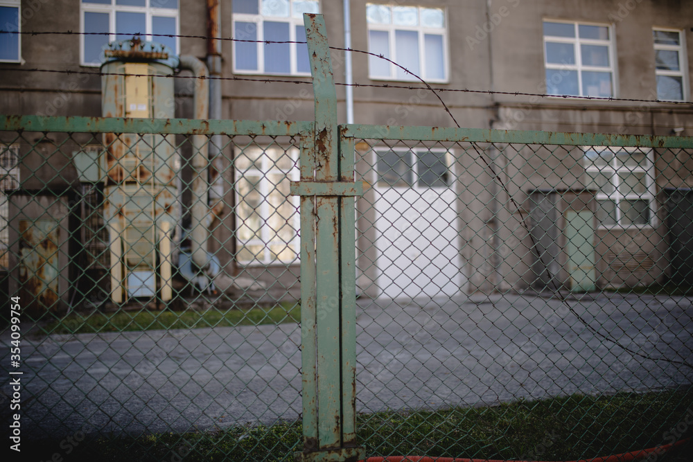 widok na stary magazyn z zewnątrz przez ogrodzenie z metalowej siatki z drutem widok na stary magazyn z zewnątrz przez ogrodzenie z metalowej siatki z drutem