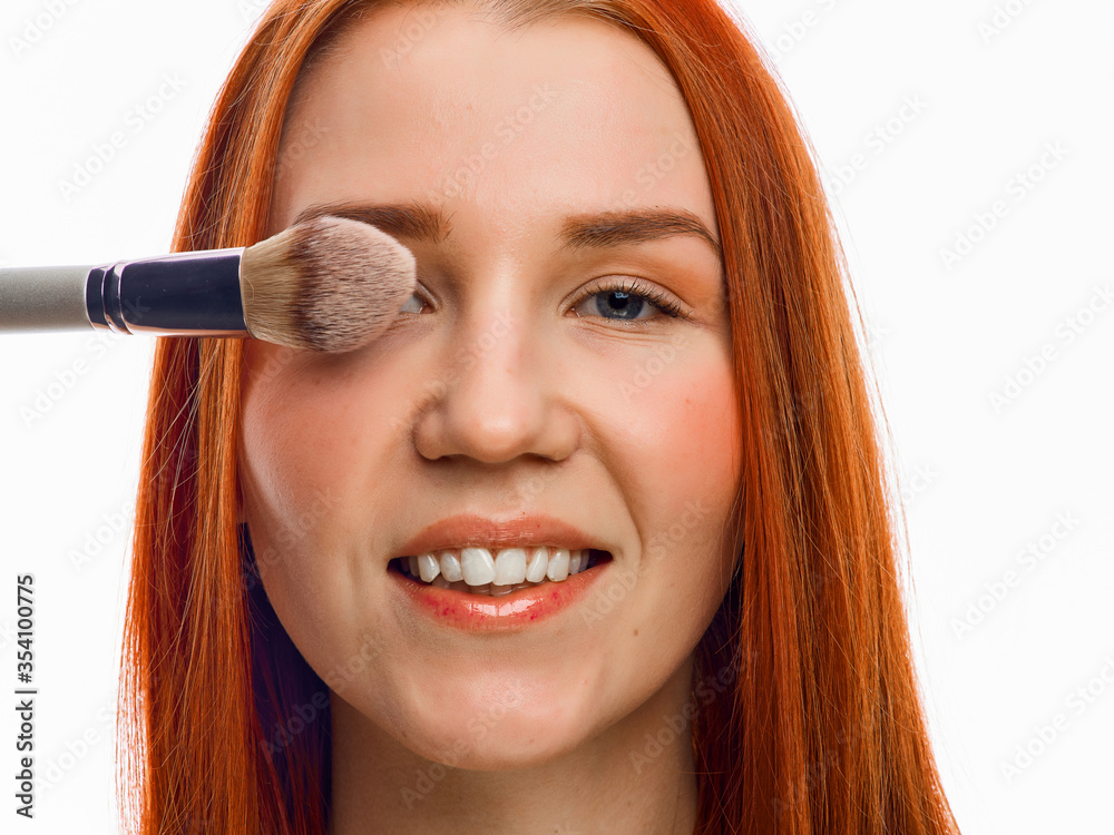 close beauty portrait of a red-haired girl with a brush for applying makeup. Isolated on a white background. close beauty portrait of a red-haired girl with a brush for applying makeup. Isolated on a white background.