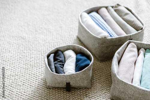 Close up of neatly folded and rolled clothes in basket. Concept of tidiness, minimalism lifestyle and japanese t-shirt folding system. Minimalist storage system photo
