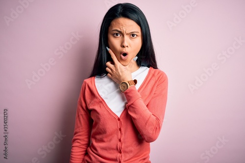 Young beautiful chinese woman wearing casual sweater over isolated pink background Looking fascinated with disbelief, surprise and amazed expression with hands on chin
