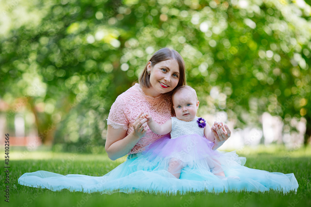 Happy mother and daughter in the park. Beauty nature scene with family outdoor lifestyle. Happy family resting together on the green grass, having fun outdoor. Happiness and harmony in family life.