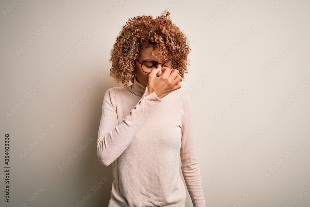 Young african american woman wearing turtleneck sweater and glasses over white background tired rubbing nose and eyes feeling fatigue and headache. Stress and frustration concept. Young african american woman wearing turtleneck sweater and glasses over white background tired rubbing nose and eyes feeling fatigue and headache. Stress and frustration concept.