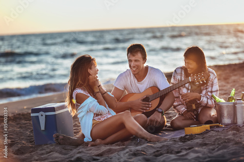 Group of friends with guitar having fun on the beach at sunset. © Mediteraneo