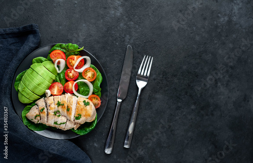  Grilled chicken breast and avocado salad with cherry tomatoes, spinach, in a black plate on a stone background with copy space for your text