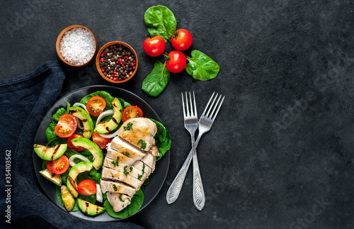 
Grilled chicken breast and grilled avocado salad with cherry tomatoes, spinach, in a black plate on a stone background 
with copy space for your text