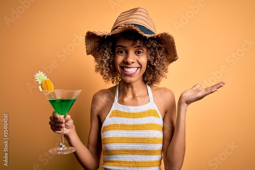 African american tourist woman with curly on vacation wearing summer hat drinking cocktail very happy and excited, winner expression celebrating victory screaming with big smile and raised hands
