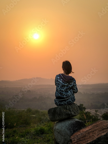 Backside shot of women sitting on the rock  looking the sunrise. © Jera