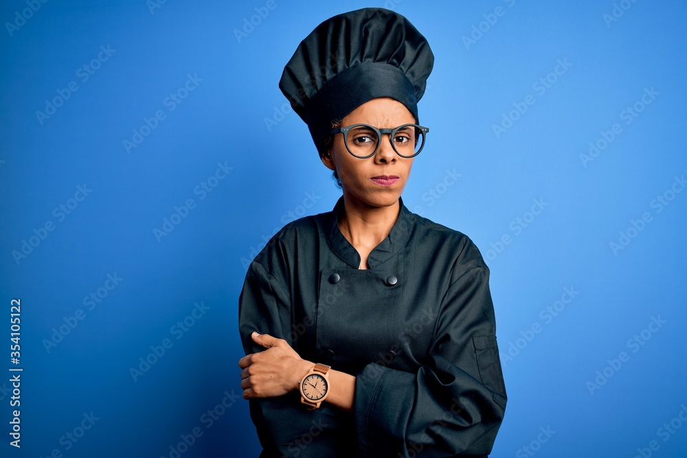 Young african american chef woman wearing cooker uniform and hat over blue background skeptic and nervous, disapproving expression on face with crossed arms. Negative person. Young african american chef woman wearing cooker uniform and hat over blue background skeptic and nervous, disapproving expression on face with crossed arms. Negative person.