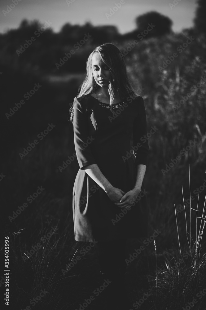 Portrait of a beautiful girl stand in autumn in dress against the background of the field on the nature. full length. look down. Close up. Black and white photo. Portrait of a beautiful girl stand in autumn in dress against the background of the field on the nature. full length. look down. Close up. Black and white photo.
