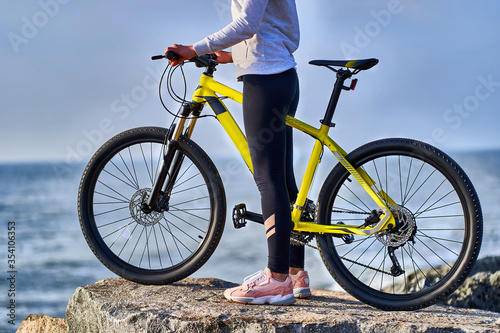 Fitness sports woman cyclist with bicycle stands on the stones on the seashore. Athletic healthy people with active and sporty lifestyle