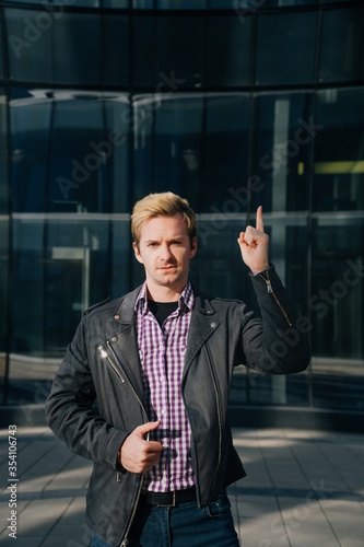 A young man in fashionable clothes points his finger up at the copy space. The concept of a joyful pointer
