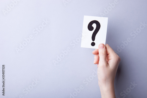 Woman holding card with question mark on color background. Paper note with question mark or sign against grey background, space for text. Ask or business concept