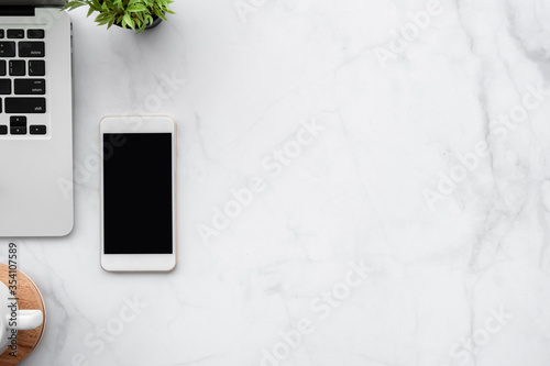 White marble office desk table with laptop computer, smartphone with blank mock up screen and supplies. Top view with copy space, flat lay.