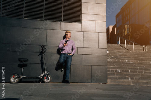 Man with smartphone and electric scooter standing near modern business center