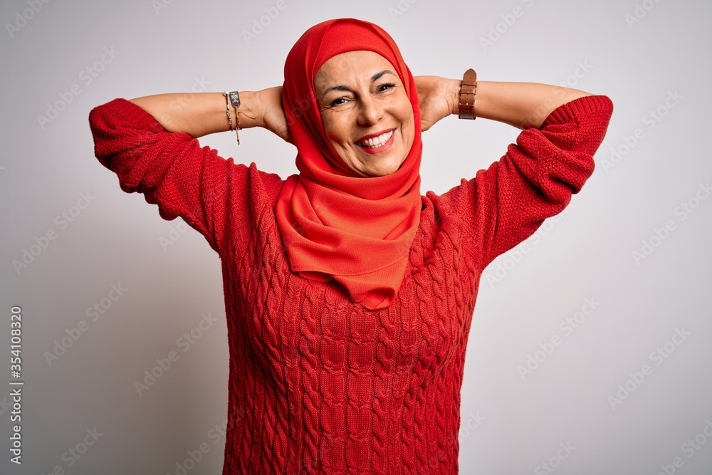 Middle age brunette woman wearing muslim traditional hijab over isolated white background relaxing and stretching, arms and hands behind head and neck smiling happy Middle age brunette woman wearing muslim traditional hijab over isolated white background relaxing and stretching, arms and hands behind head and neck smiling happy