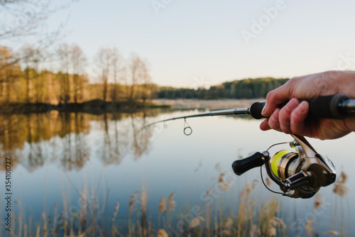 A fisherman with a fishing rod in his hand catches a fish on the shore of a lake or river. Fishing Day. Spinning in hand on pond background.