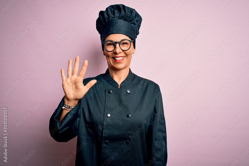 Middle age brunette chef woman wearing cooker uniform and hat over isolated pink background showing and pointing up with fingers number five while smiling confident and happy. Middle age brunette chef woman wearing cooker uniform and hat over isolated pink background showing and pointing up with fingers number five while smiling confident and happy.