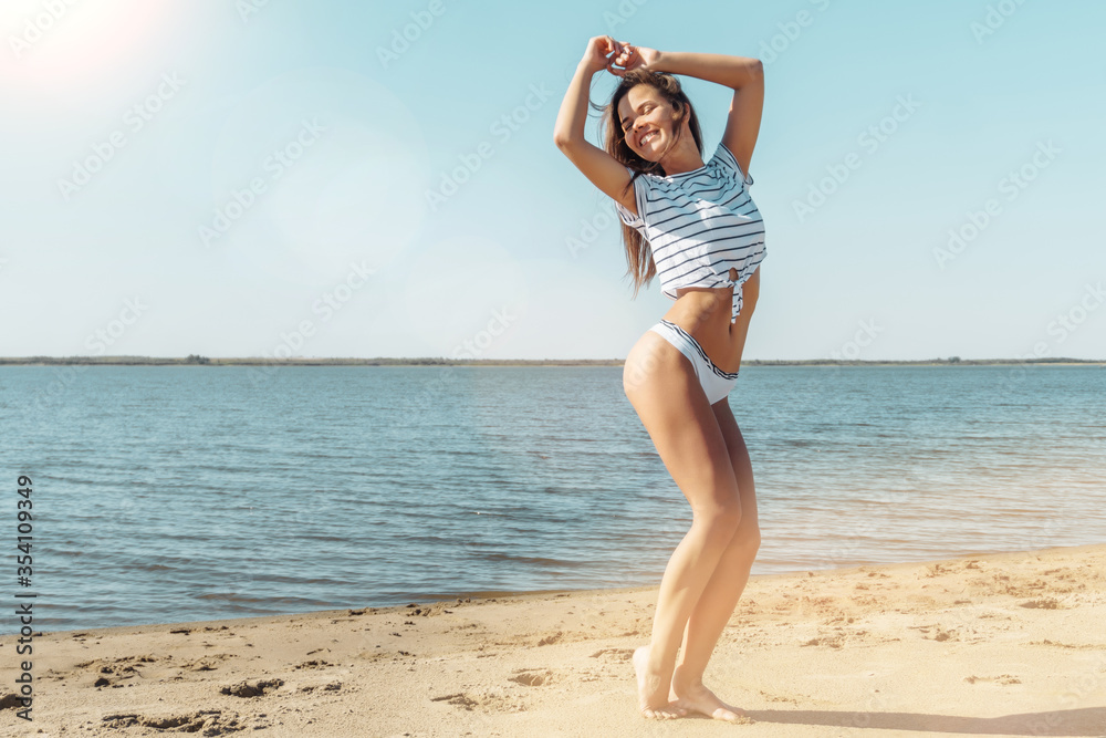 Young attractive brunette woman in white striped shirt and thong enjoying the summer with sea on background Young attractive brunette woman in white striped shirt and thong enjoying the summer with sea on background