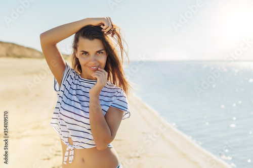 Young attractive brunette woman in white striped shirt enjoying the summer with sea on background