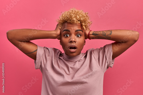 Shocked scared african american young student female clutching her head in panic, missing graduation project deadline on a pink background. Concept of total discounts and black Friday in the store photo