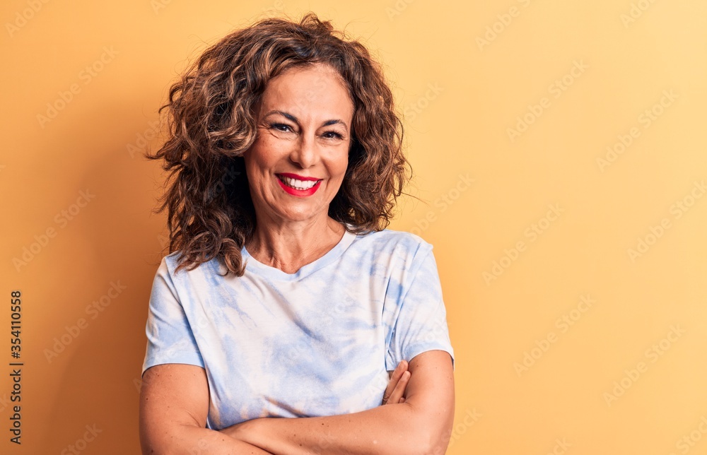 Middle age beautiful woman wearing casual dye t-shirt standing over yellow background happy face smiling with crossed arms looking at the camera. Positive person. Middle age beautiful woman wearing casual dye t-shirt standing over yellow background happy face smiling with crossed arms looking at the camera. Positive person.