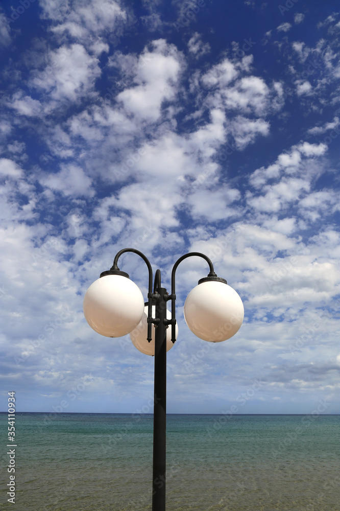 Street lamp against the blue sky with white clouds and sea Street lamp against the blue sky with white clouds and sea