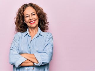 Middle age beautiful woman wearing casual denim shirt standing over pink background happy face smiling with crossed arms looking at the camera. Positive person.