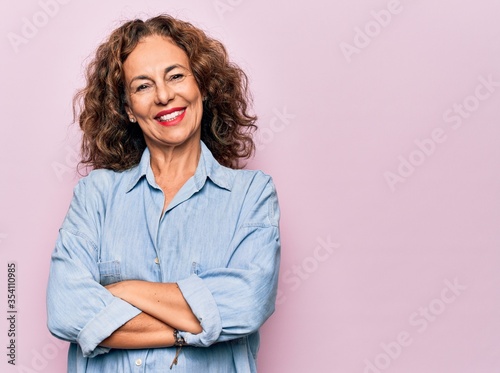 Fotografie, Obraz Middle age beautiful woman wearing casual denim shirt standing over pink background happy face smiling with crossed arms looking at the camera