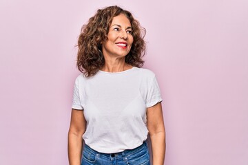 Middle age beautiful woman wearing casual t-shirt standing over isolated pink background looking to side, relax profile pose with natural face and confident smile.