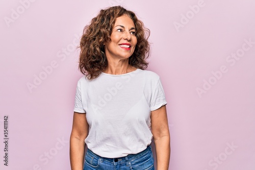 Middle age beautiful woman wearing casual t-shirt standing over isolated pink background looking to side, relax profile pose with natural face and confident smile.