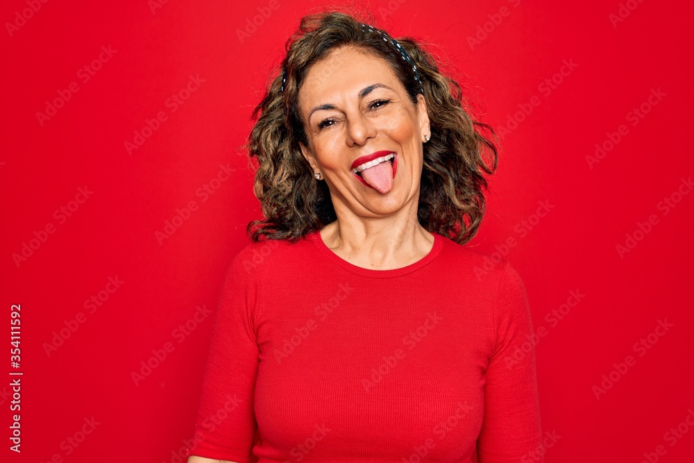 Middle age senior brunette woman wearing casual t-shirt standing over red background sticking tongue out happy with funny expression. Emotion concept. Middle age senior brunette woman wearing casual t-shirt standing over red background sticking tongue out happy with funny expression. Emotion concept.