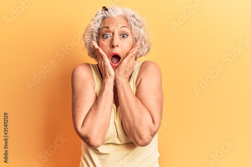 Senior grey-haired woman wearing casual clothes afraid and shocked, surprise and amazed expression with hands on face