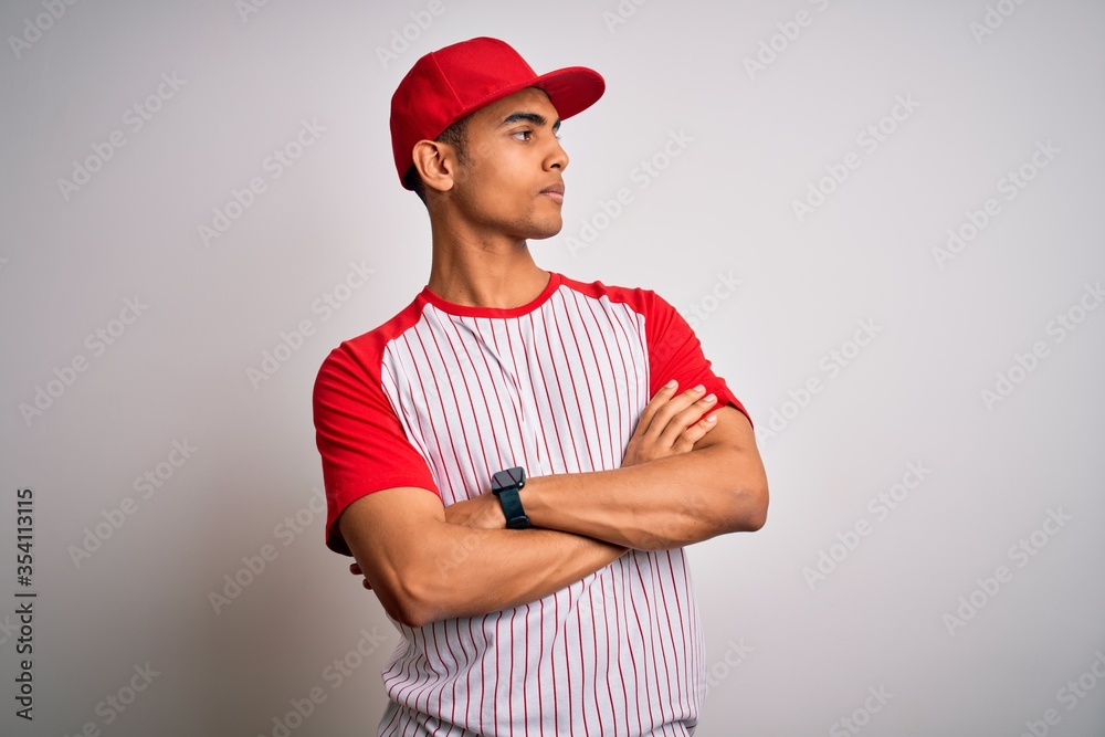 Young handsome african american sportsman wearing striped baseball t-shirt and cap looking to the side with arms crossed convinced and confident Young handsome african american sportsman wearing striped baseball t-shirt and cap looking to the side with arms crossed convinced and confident