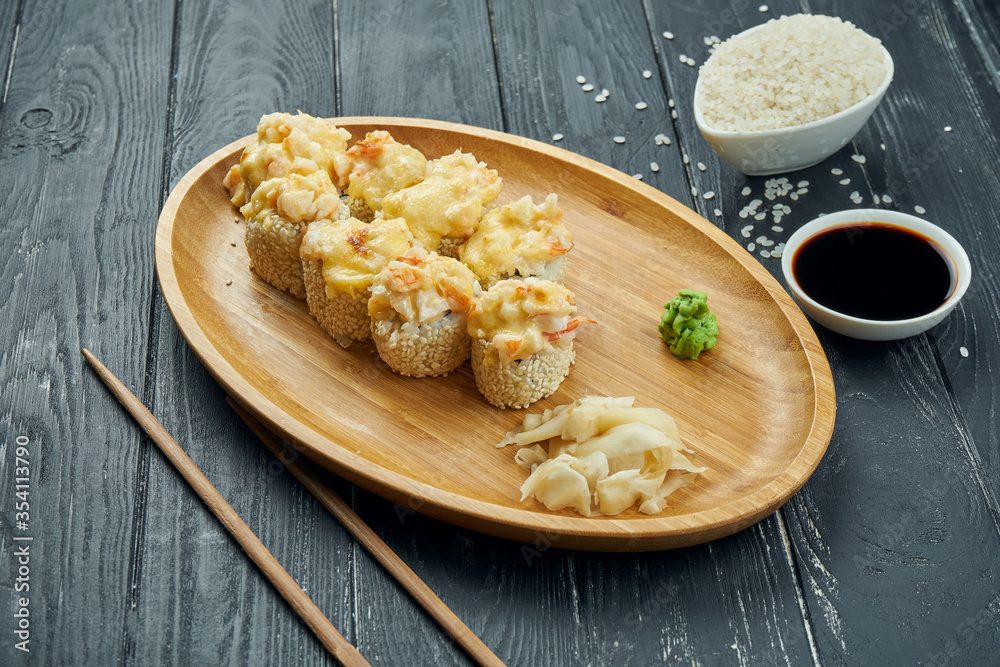 Classic japanese sushi rolls - baked rolls with cream cheese, spicy sauce and shrimp on a bamboo plate on a black wooden background Classic japanese sushi rolls - baked rolls with cream cheese, spicy sauce and shrimp on a bamboo plate on a black wooden background