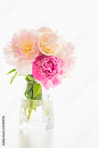 Pink peonies close up on white background. Elegant bouquet in glass vase. Vertical banner