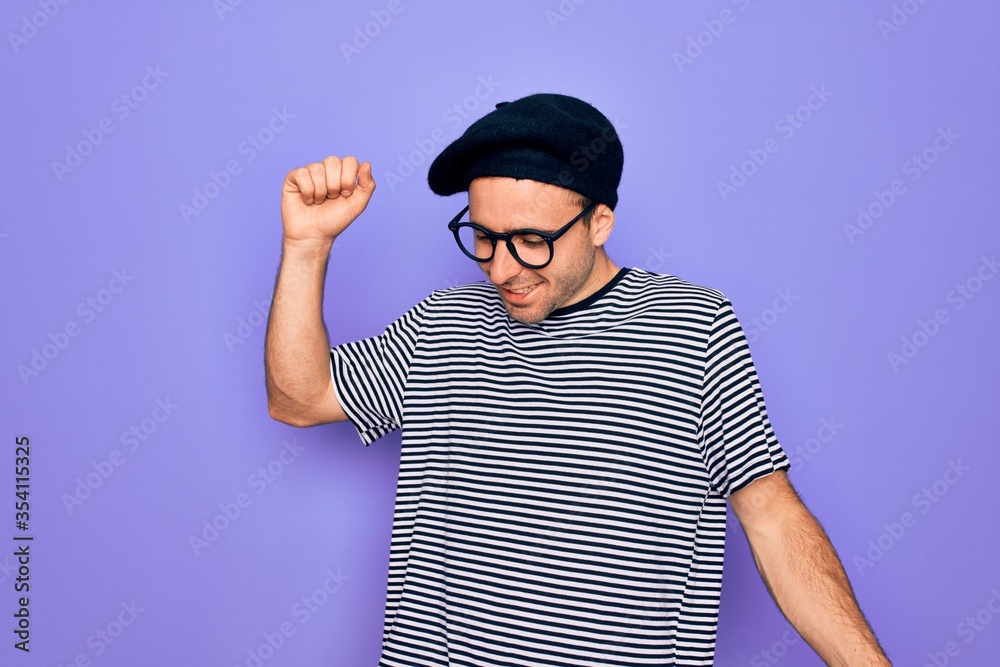 Handsome man with blue eyes wearing striped t-shirt and french beret over purple background Dancing happy and cheerful, smiling moving casual and confident listening to music Handsome man with blue eyes wearing striped t-shirt and french beret over purple background Dancing happy and cheerful, smiling moving casual and confident listening to music