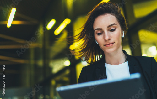 portrait professional female manager looking on screen tablet standing near office in evening street. Businesswoman using computer on background yellow neon lights