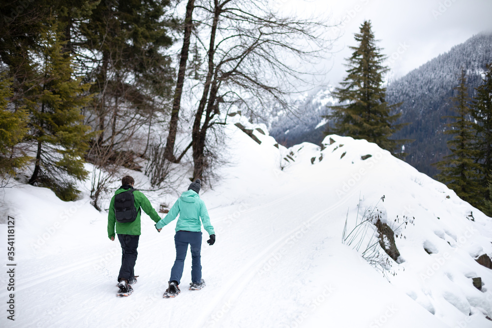 Snowshoeing couple holding hands and walking along a snowy mountain trail, with space for text on the right