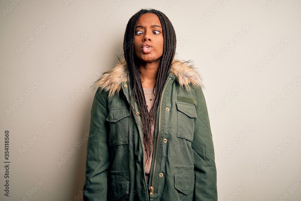 Young african american woman wearing winter parka coat over isolated background making fish face with lips, crazy and comical gesture. Funny expression. Young african american woman wearing winter parka coat over isolated background making fish face with lips, crazy and comical gesture. Funny expression.