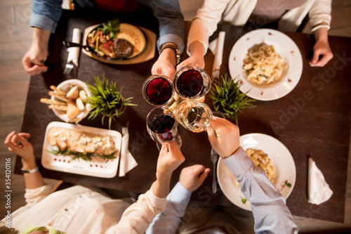 Four hands with red wine toasting over served table with food
