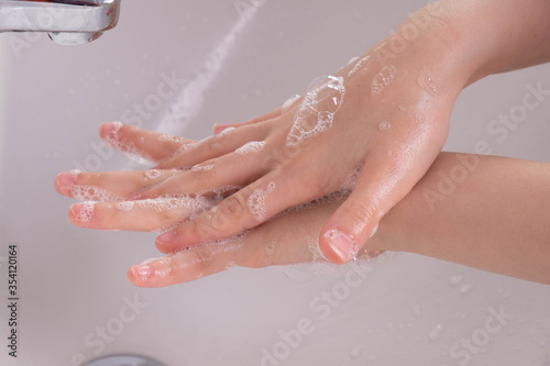 young girl soaped her hands and holds them under the tap in the bathroom