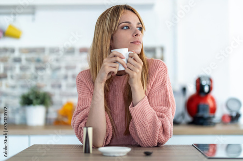 Thoughtful young woman drinking coffee on the kitchen in the morning.
