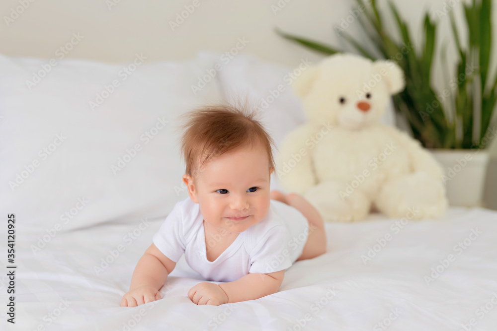 Newborn baby girl resting in bed. Family morning at home. Infant lies on his stomach in bed with a teddy bear Newborn baby girl resting in bed. Family morning at home. Infant lies on his stomach in bed with a teddy bear