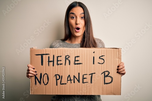 Young beautiful brunette activist woman protesting for save the planet holding banner scared in shock with a surprise face, afraid and excited with fear expression © Krakenimages.com