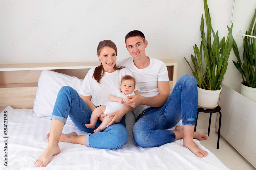 Happy family: father, mother and baby son play on a white bed in a sunny bedroom. Family having fun together, hugging each other. Happy family: father, mother and baby son play on a white bed in a sunny bedroom. Family having fun together, hugging each other.