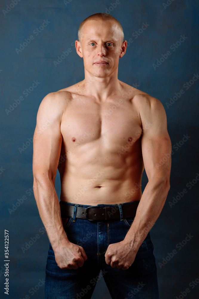 Obraz premium Portrait of strong healthy handsome Athletic Man Fitness Model posing near dark blue wall