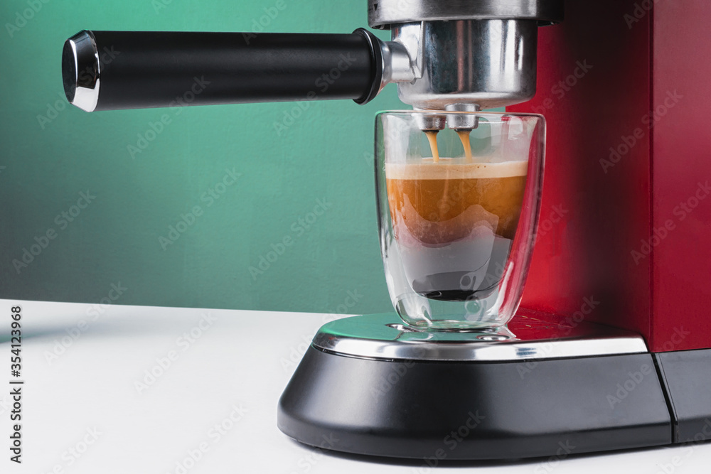 Red coffee machine. Transparent glass mug with fresh coffee. Coffee holder and cappuccino maker Red coffee machine. Transparent glass mug with fresh coffee. Coffee holder and cappuccino maker