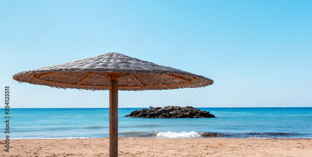 Beach umbrella, view of the sandy seashore, sea, stone island and blue sky. Perfect beach holiday concept. Travel and vacation. Seascape. Chalikounas Beach, Corfu Island. Copy space