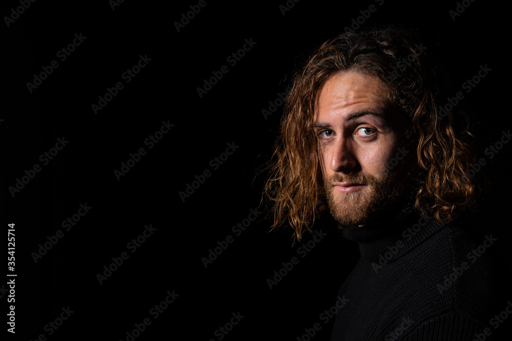 attractive man with long hair with blue eyes looking at camera on black background